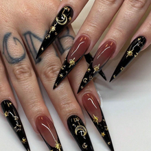 Load image into Gallery viewer, Extra long stiletto nails with deep nude base and black french and solid nails. Gold star and moon designs all over.
