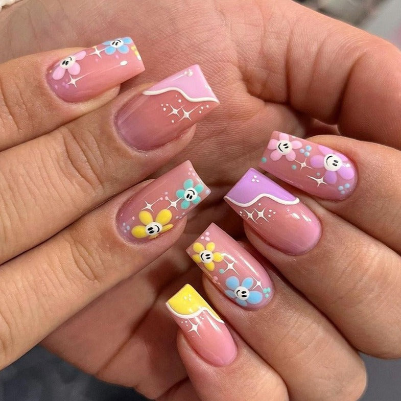 medium coffin fake nails with pastel colors and smile faces inside of flowers. 